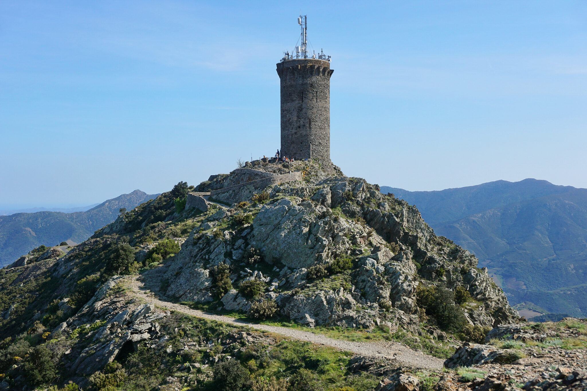 Tour de guet en pierre, collines, antennes, ciel bleu.