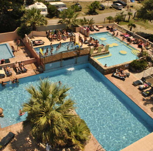 Vue aérienne de campings Arlequin Vacances avec piscines, vacanciers et palmiers, été.
