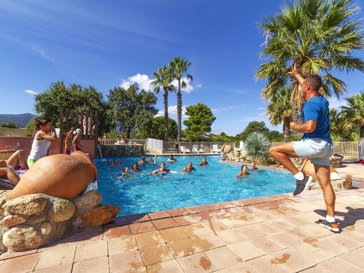 Animateur dirige un cours aquatique convivial au camping Arlequin Vacances, piscine entourée de palmiers.
